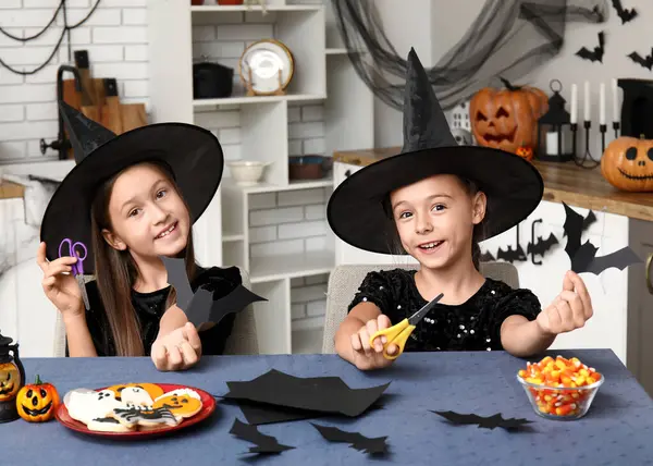 Cadılar Bayramı için giyinmiş şirin kızlar mutfakta yarasa kesen cadılar gibi.