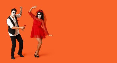 Meksika Ölüler Günü 'nde (El Dia de Muertos) yüzlerinde boyalı kafatasları olan dans eden genç bir çift, turuncu arka planda mesajlaşmak için boşluk yaratıyor.