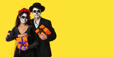 Meksika Ölüler Günü (El Dia de Muertos) için giyinmiş genç bir çift sarı arka planda mesajlaşma için alan ve hediyeler taşıyorlar.