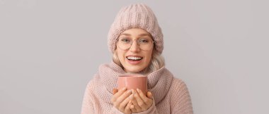 Gri arka planda çay içen kalın elbiseli güzel bir genç kadın.