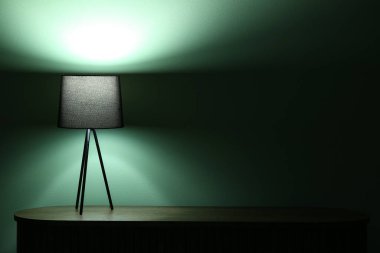 Karanlık odadaki ahşap masada parlayan lamba.