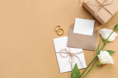 Hediye kutulu kompozisyon, boş kartlar, zarf, alyanslar ve bej arka planda güzel östoma çiçekleri.