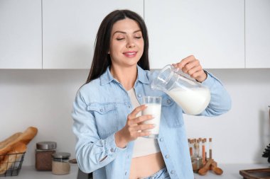 Güzel bir kadın mutfakta bardağa süt dolduruyor.