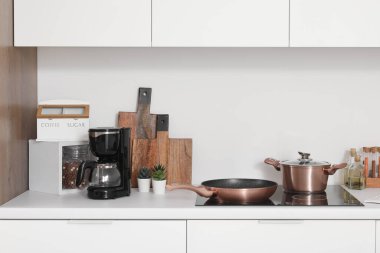 Elektrikli ocağı olan beyaz mutfak tezgahı, kızartma tavası, tencere ve çatal bıçak.