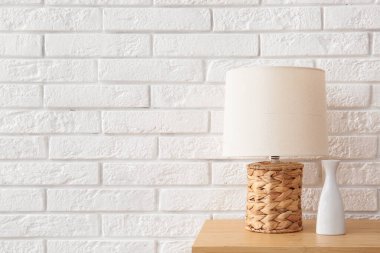 Lamba ve seramik vazo beyaz tuğla duvarın yanındaki ahşap masada.