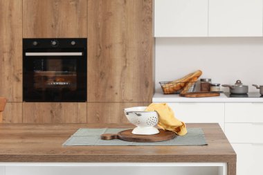 Modern mutfağın içinde kevgir ve tahta kesme tahtaları olan ahşap bir ada masası.