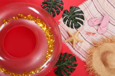 Kırmızı arka planda plaj aksesuarları olan şişme bir yüzük.