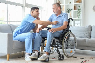 Erkek hemşire, evde steteskoplu tekerlekli sandalyedeki yaşlı adamı duyuyor.