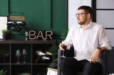 Genç şarap bardağıyla oturma odasında siyah koltukta oturan şarap garsonu.