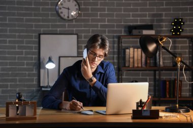 Genç işadamı cep telefonuyla konuşuyor ve geceleri ofiste çalışıyor.