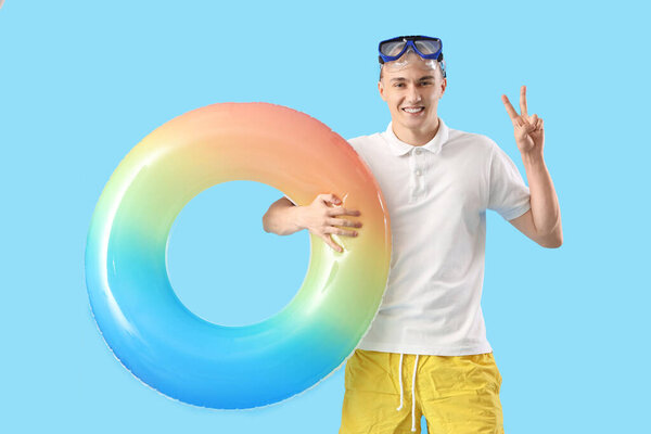 Молодой человек в маске для подводного плавания и плавания кольцо с победным жестом на синем фоне