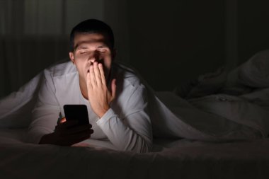 Uykulu genç adam geceleri cep telefonu kullanıyor.