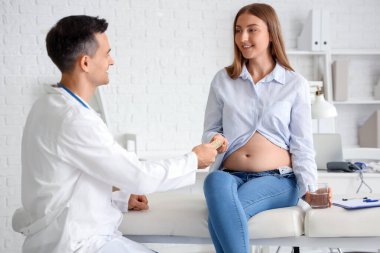 Erkek doktor klinikteki hamile kadına hap veriyor.