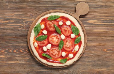 Domates soslu pizza hamuru ve ahşap arka planda malzemeler.