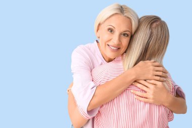 Mutlu genç bir kadın, annesi mavi arka planda sarılıyor.