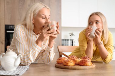 Güzel genç bir kadın ve annesi mutfakta lezzetli çöreklerle çay içiyorlar.