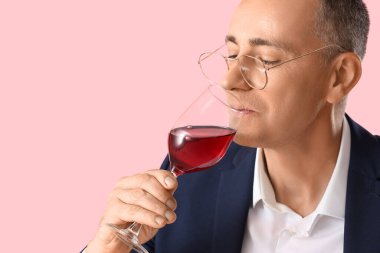 Olgun bir adam pembe arka planda kırmızı şarap tadıyor, yakın plan.