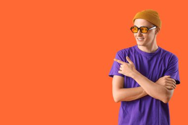 Güneş gözlüklü genç adam kırmızı arka planda bir şeye bakıyor.