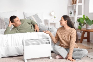 Yatak odasındaki radyatörün yanında ısınan genç çift.