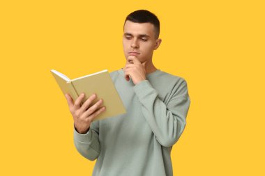 Düşünceli genç adam sarı arka planda kitap okuyor.