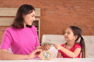 Annesiyle küçük bir kız evdeki domuz kumbarasına para yatırıyor.