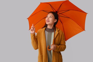 Gri arka planda şemsiyeyi gösteren güzel bir Asyalı kadın.