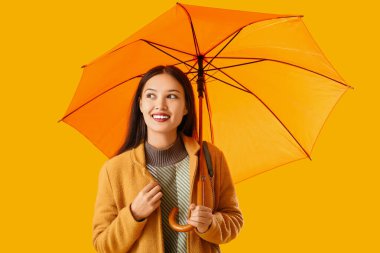 Sarı arka planda şemsiyesi olan güzel bir Asyalı kadın.