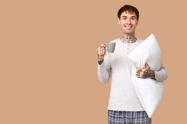 Kahverengi arka planda yastıklı ve kahveli pijamalı dövmeli genç adam.