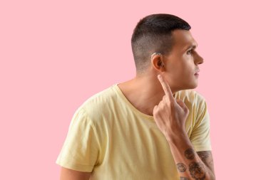 Pembe arka planda işitme cihazına işaret eden genç adam