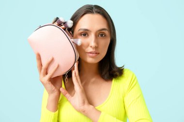 Mavi arka planda makyaj ürünleriyle dolu kozmetik çantası olan güzel genç bir kadın.