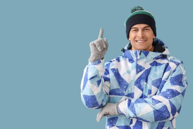 Kışın giyinmiş yakışıklı adam mavi arka plandaki bir şeyi işaret ediyor.