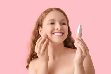 Makyaj temeli ve pembe arka planda süngeri olan genç kızıl saçlı kadın, yakın plan.