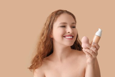 Makyaj temeli ve bej arka planda süngeri olan genç kızıl saçlı kadın, yakın plan.