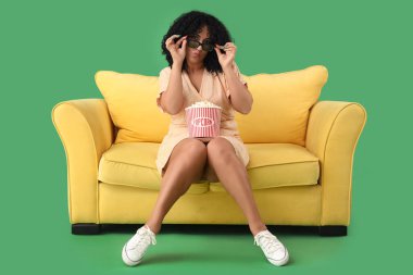 Üç boyutlu gözlüklü, patlamış mısırlı güzel bir kadın yeşil arka planda film izliyor.