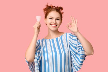 Regl fincanı olan güzel genç bir kadın pembe arka planda güzel bir jest gösteriyor.