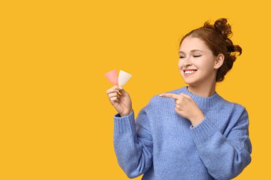 Güzel genç bayan sarı arka plandaki regl bardaklarını gösteriyor.