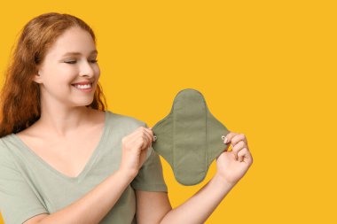 Sarı arka planda tekrar kullanılabilir adet pedi olan güzel genç bir kadın.