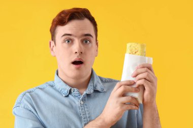 Sarı arka planda lezzetli sandviçli şaşkın genç adam, yakın plan