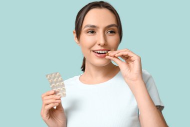 Güzel genç bayan mavi arka planda haplar alıyor.