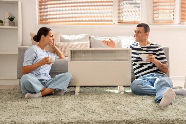 Young couple with tea warming near radiator at home