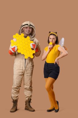 Male beekeeper with paper honeycombs and woman in bee costume on brown background clipart