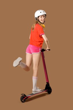 Kasklı güzel bir kadın kahverengi arka planda modern elektrikli scooter kullanıyor.