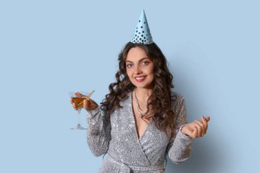 Doğum günü şapkalı ve açık mavi arka planda kokteyli olan genç bir kadın.