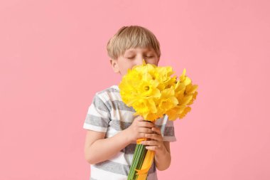 Cute little happy boy with bouquet of beautiful narcissus on pink background