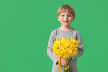 Cute little happy boy with bouquet of beautiful narcissus on green background