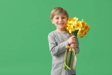 Cute little happy boy with bouquet of beautiful narcissus on green background