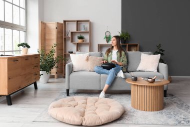 Evdeki kanepede glukofon çalan genç bir kadın.