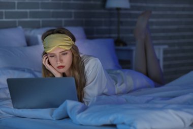 Geceleri yatak odasında dizüstü bilgisayar kullanan uykusuzluk çeken genç bir kadın.