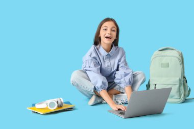 Küçük liseli kız mavi arka planda dizüstü bilgisayarla çalışıyor.