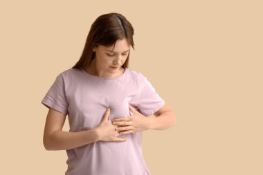 Bej arka planda göğüslerini kontrol eden genç bir kadın.